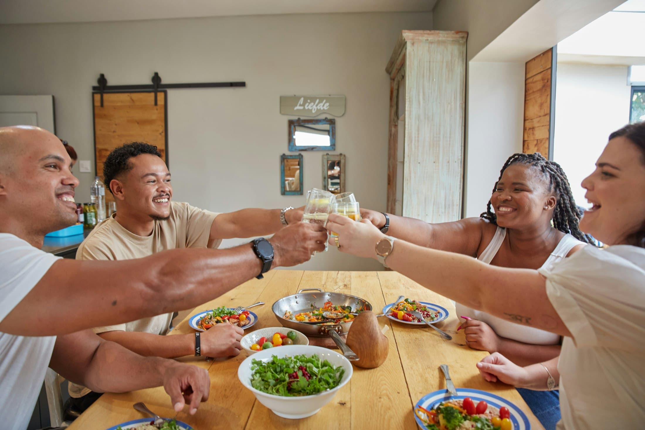 Friends toasting with juice and water over a colorful home-cooked dinner at a modern kitchen table